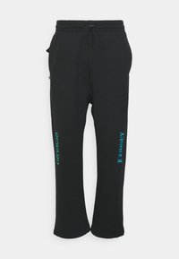 Schwarze Sweatpants aus weichem Stoff, mit lockerer Passform, Kordelzugbund und türkisfarbenem Text mit den Aufdrucken "REWARD" und "JOURNEY" an den Seiten.