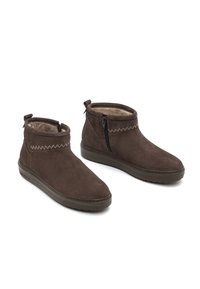Botines de ante marrón con cierre de cremallera, parte superior texturizada y forro suave. Presentan un diseño de costura elevada y una suela plana de goma.