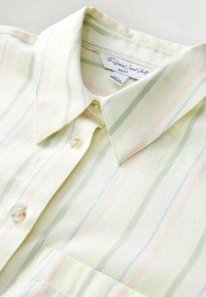 Gaiši dzeltena krekla tipa krekls ar vertikālām pasteliski zaļām, zilām un rozā svītrām. Aprīkots ar punktētu apkakli un vienu priekšējo kabatu.