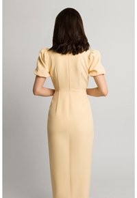 Żółta sukienka z bufiastymi rękawami, dopasowana sylwetka i gładka tekstura. Posiada przeszywane szwy z tyłu i długość do kolan.