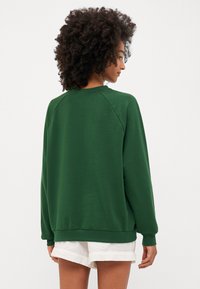 Groen sweatshirt met een losse pasvorm, raglanmouwen en geribbelde manchetten. Soepele textuur; halflang en minimalistisch ontwerp.