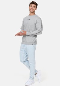 Gray sweatshirt with logo on chest and sleeve, paired with light blue pants and white sneakers. Casual fit and soft fabric texture.