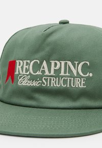 Grønn caps med strukturert design, med hvit brodering av "RECAPINC. Classic STRUCTURE" og en rød aksentlogo. Glatt tekstur.