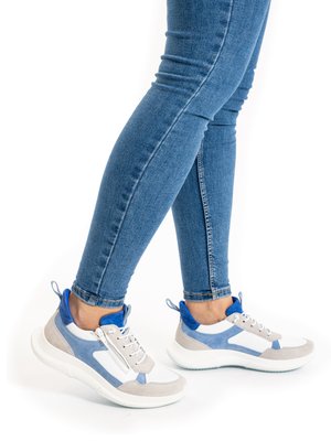Legs wearing blue skinny jeans and white sneakers with blue and gray accents, standing on a white background.