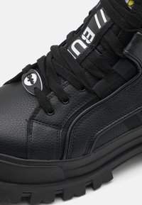 Black high-top sneakers with textured leather, thick rubber sole, black laces, metal accents, and white logo detailing on the tongue.
