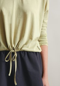 Lichtgroen top met een gebundelde taille en trekkoorddetails, gecombineerd met een donkeren marineblauwe rok. Zachte stof met een losse pasvorm.