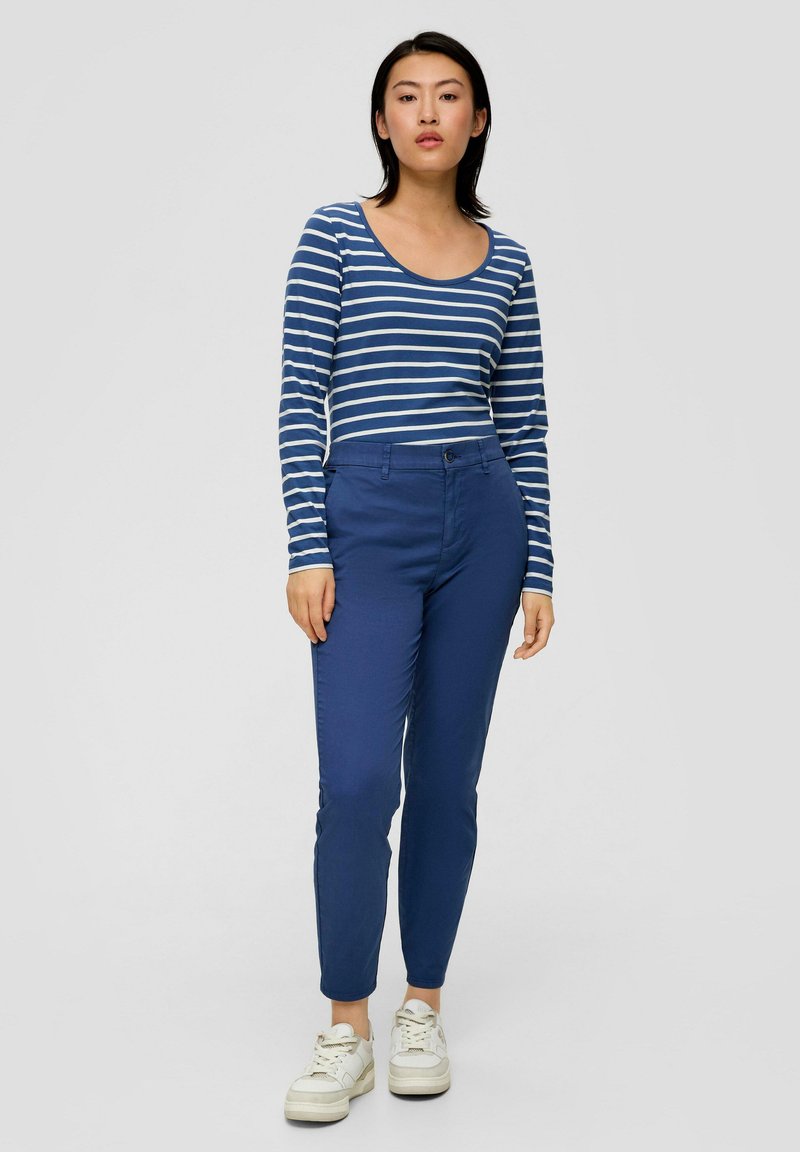 Gestreiftes langärmliges Oberteil in Blau und Weiß, kombiniert mit schmal geschnittenen blauen Hosen und weißen Sneakern. Mit Rundhalsausschnitt und minimaler Ausstattung.