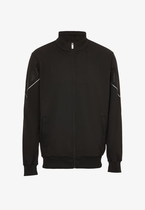 Fekete, cipzáros dzseki puha anyagból, magas gallérral, két oldalsó zsebbel, bordázott mandzsettákkal és diszkrét fehér részletekkel a vállakon.