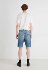 Denim šorti, gaiši zili, novalkāts apmale, divas aizmugurējās kabatas ar šuvju detaļām, kopā ar baltu īsu piedurkņu T-kreklu un melniem apaviem.