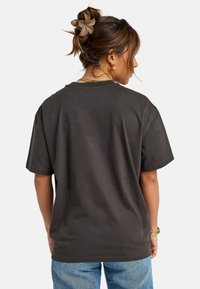 Camiseta de algodón gris oscuro de manga corta, de corte relajado y con cuello redondo, combinada con unos vaqueros de mezclilla azul claro. Sin patrones ni acentos notables.