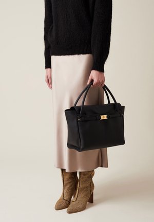 Borsa a tracolla in pelle nera con un design rettangolare strutturato, dettagli in metallo dorato e manici robusti, abbinata a una gonna in satin beige e stivali texture.