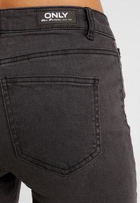 Vaqueros de mezclilla negros con vista trasera, dos bolsillos, detalles cosidos y una etiqueta que dice "ONLY". Diseño ajustado y texturizado.