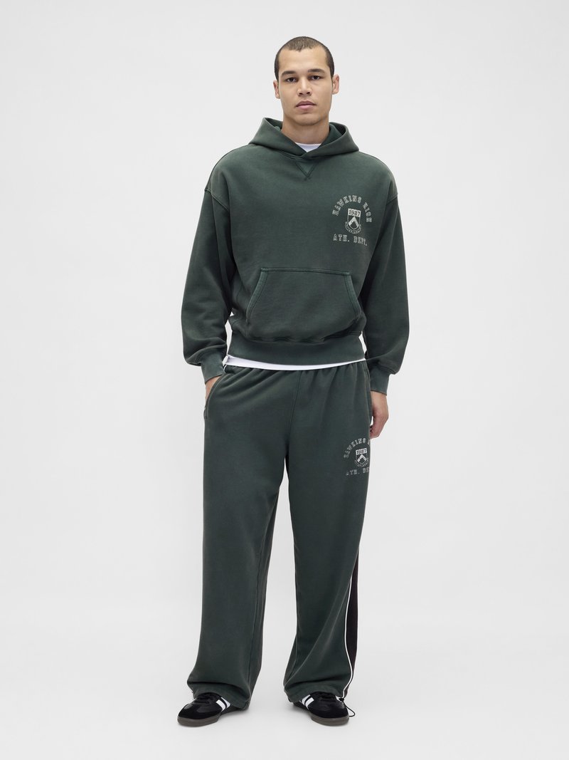 Olive green hooded sweatshirt with front pocket, paired with matching wide-leg sweatpants featuring white side stripes and graphic print accents.