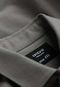 Polo gris avec une texture lisse, doté d'un col et d'une étiquette noire indiquant "ombre menswear taille M."