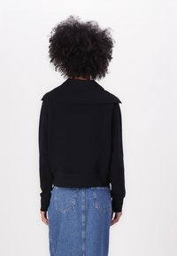 Black sweatshirt with a wide collar, cropped design, and ribbed cuffs, paired with a denim skirt featuring a straight silhouette and back pockets.