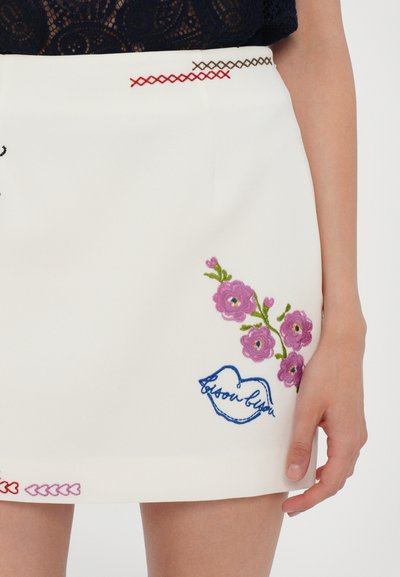White skirt featuring colorful floral embroidery in pink and green, accented with blue stitching forming a stylized heart and text.