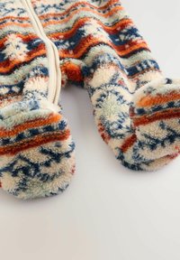 Un onesie en polaire coloré et texturé avec un motif en zigzag orange, bleu et crème, mettant l'accent sur le design confortable à pieds et la fermeture éclair à l'avant.