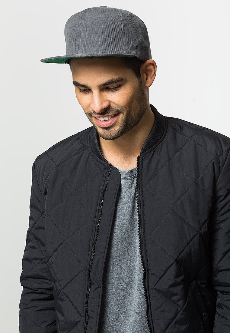 Black quilted bomber jacket over a gray t-shirt, paired with a gray cap featuring a green brim. Clean design with no visible logos.