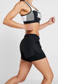 Svarta idrottsshorts med elastisk midja och sidoflikar, kombinerat med en grå och vit sportbh med en framträdande logotyp.