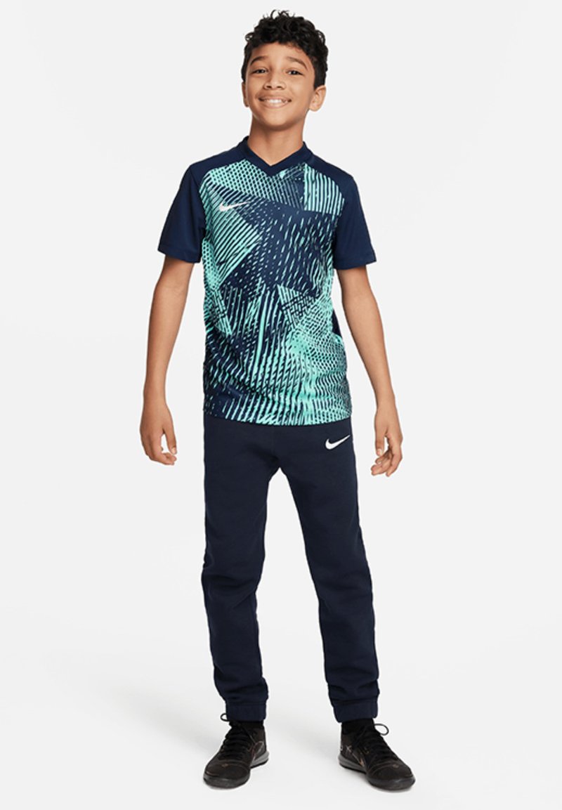 Jongens sportoutfit met een blauw-groen grafisch patroon op een T-shirt met korte mouwen en marineblauwe trainingsbroek met een Nike-logo.