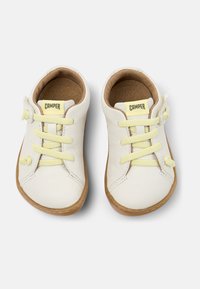 Scarpe in pelle bianca con lacci gialli, punta arrotondata e suola in gomma beige. Presentano una piccola etichetta con logo e semplici dettagli di cucitura.