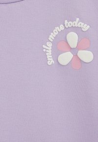 Fialovo-bavlnená mikina s textúrovanou bielou kvetinovou aplikáciou s ružovými akcentmi a vyšitým textom: "usmievaj sa viac dnes."