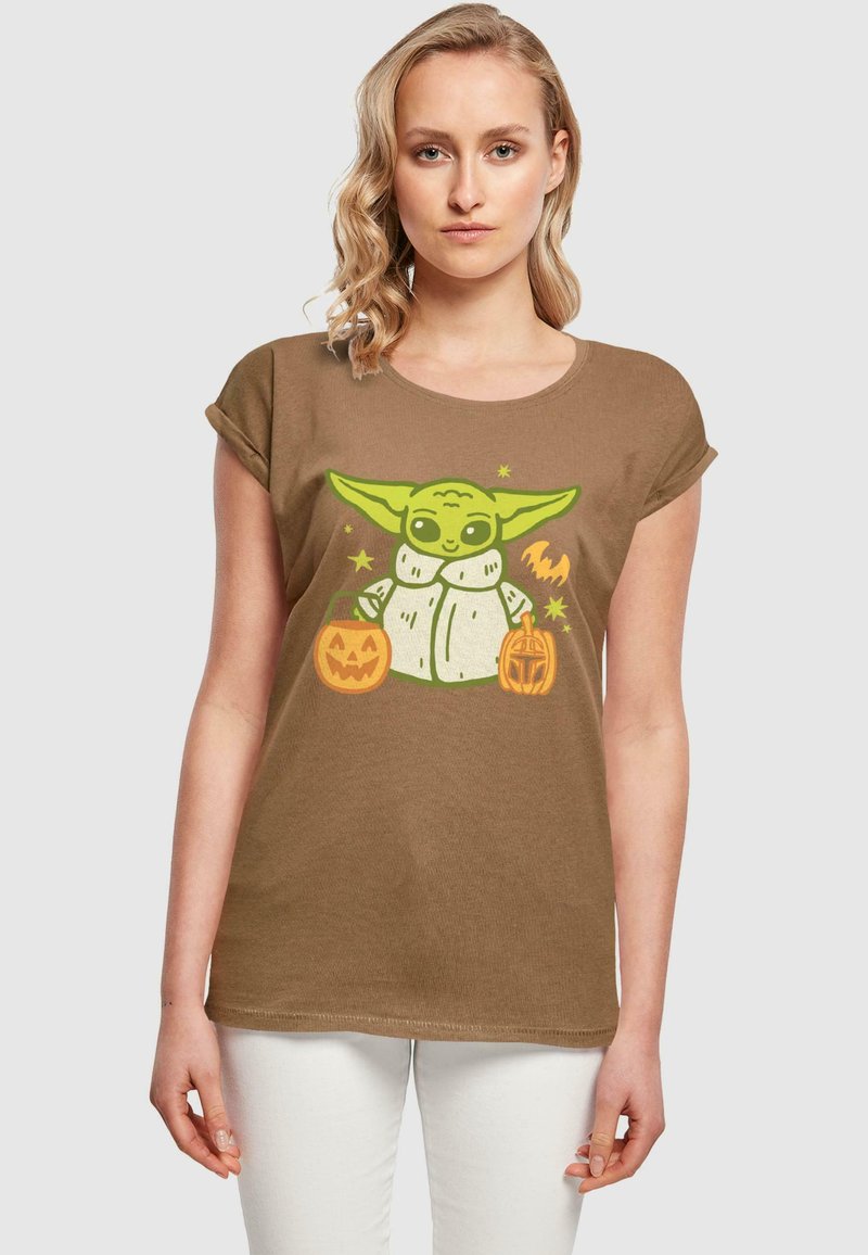Brun kortärmad t-shirt med en grön karaktär som håller två Halloween-pumpor, med grafiska detaljer och en avslappnad passform.