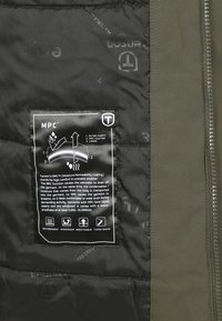 Waterdichte jas met olijfgroene buitenstof, zwarte binnenvoering en een gelabelde tag met details over de vochtigheidsdoorlatende coating en kenmerken.