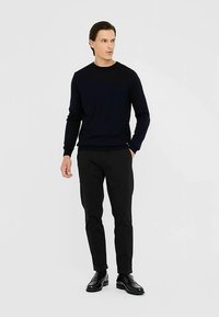 Džemper tamnoplave boje s okruglim izrezom, uparен s crnim uskim hlačama i crnom obućom, s glatkom teksturom tkanine na cijelom predmetu.