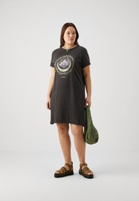 Pelēka kokvilnas T-kreklu kleita ar lotosa grafiku un trajektoriju dizainu, īsām piedurknēm un brīvu piegriezumu, apvienota ar olīvu zaļām sandalēm un somu.