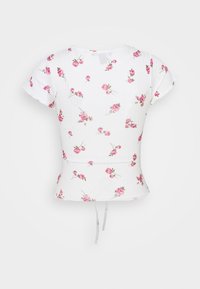 Vit kortärmad topp med rosa blommönster, ribbad textur, figursydd midja och knyt-detalj i nederkant.