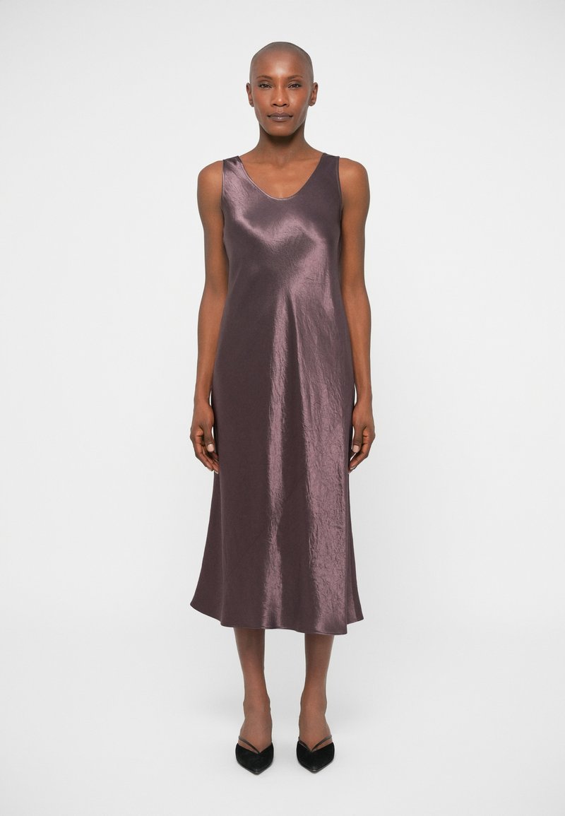 Satin, ärmelloses Midikleid in tiefem Pflaumenfarbe mit leichtem Glanz. Fließende Silhouette und V-Ausschnitt-Design, kombiniert mit spitzen schwarzen Absätzen.