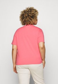 Camiseta de manga corta color coral, hecha de tela suave, con cuello redondo y ajuste relajado, combinada con pantalones beige claros.