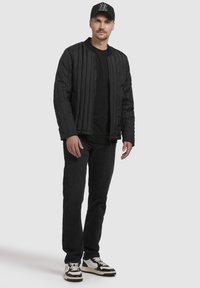 Black quilted bomber jacket with vertical stitching, worn over a black shirt. Paired with dark jeans and black-and-white sneakers.