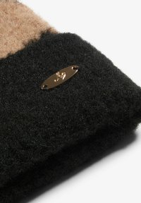 Mustat huopatuotteet, joissa on sileä, teksturoitu pinta ja kiiltävä kultainen metallilevy, johon on sijoitettu tyylitelty logo.