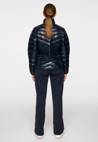 Granatowa kurtka puchowa o dopasowanym kroju, z pionowym pikowaniem i wysokim kołnierzem. Tył zdobiony marszczeniami. W połączeniu z ciemnymi spodniami i trampkami.