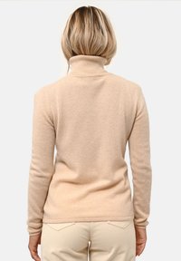 Pullover a collo alto beige chiaro realizzato in tessuto morbido, con maniche lunghe e design aderente, caratterizzato da una superficie liscia e colletto a coste.