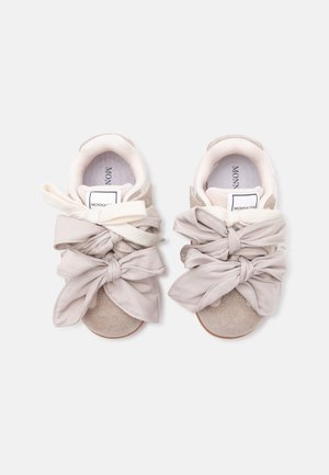 Paire de baskets en daim beige avec de grands nœuds en tissu noués et une doublure intérieure blanche, vues de dessus sur un fond clair.