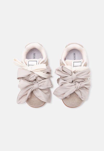 Paire de baskets en daim beige avec de grands nœuds en tissu noués et une doublure intérieure blanche, vues de dessus sur un fond clair.