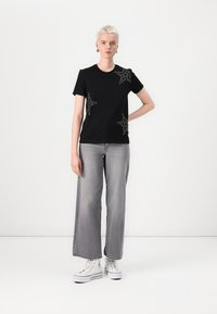 Black cotton t-shirt with silver star designs on the front, paired with wide-leg gray denim jeans and white high-top sneakers.