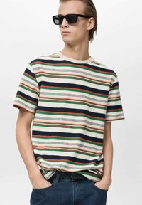 T-shirt à manches courtes rayé en crème, avec des bandes rouges, vertes et bleu marine. Design à col rond avec une coupe décontractée, associé à un jean foncé.