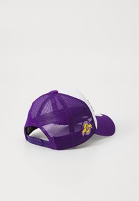 Căciulă din plasă purpurie cu un panou frontal alb, vizieră curbă, curea ajustabilă și un patch cu logo pe lateral. Material texturat și culori vibrante.