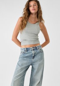Grijze geribbelde tanktop met een fitted ontwerp, gecombineerd met lichtblauwe high-waisted spijkerbroek met een gebloemde tailleband.