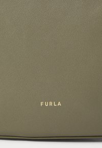 Borsa a mano in pelle verde con una texture liscia. Presenta un logo dorato "Furla" nella parte inferiore. Design semplice e rettangolare.