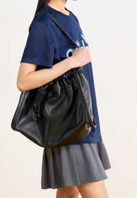 Svart läderpåse med dragsnodd och en mjuk, slät textur. Väskan har en avslappnad form och bärs på axeln.