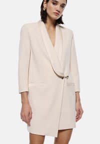 Vestito blazer color pesca con colletto a scialle, chiusura con un solo bottone e due tasche frontali. Tessuto liscio con forma strutturata e maniche lunghe.