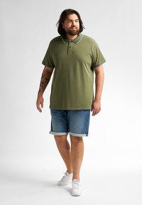 Zielona koszulka polo z niebiesko-białym kołnierzykiem, w połączeniu z dżinsowymi szortami. Casualowe obuwie dopełnia strój.