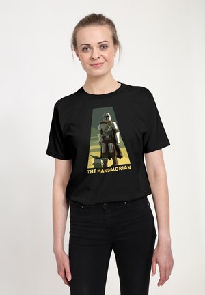 Kvinde iført sort T-shirt med stiliserede Mandalorian- og Grogu-figurer samt teksten "The Mandalorian" på fronten.
