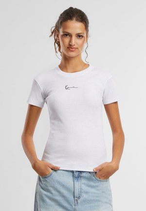 Hvit tettsittende t-skjorte med korte ermer, ribbestruktur og en svart signaturlogo på brystet. Kombinert med lyseblå jeans.