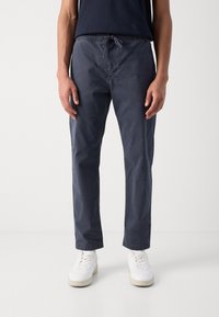 Mörkblå elastiska midjebyxor med dragsko, rak ben-design, lättviktsmaterial och två sidofickor, i kombination med vita sneakers.